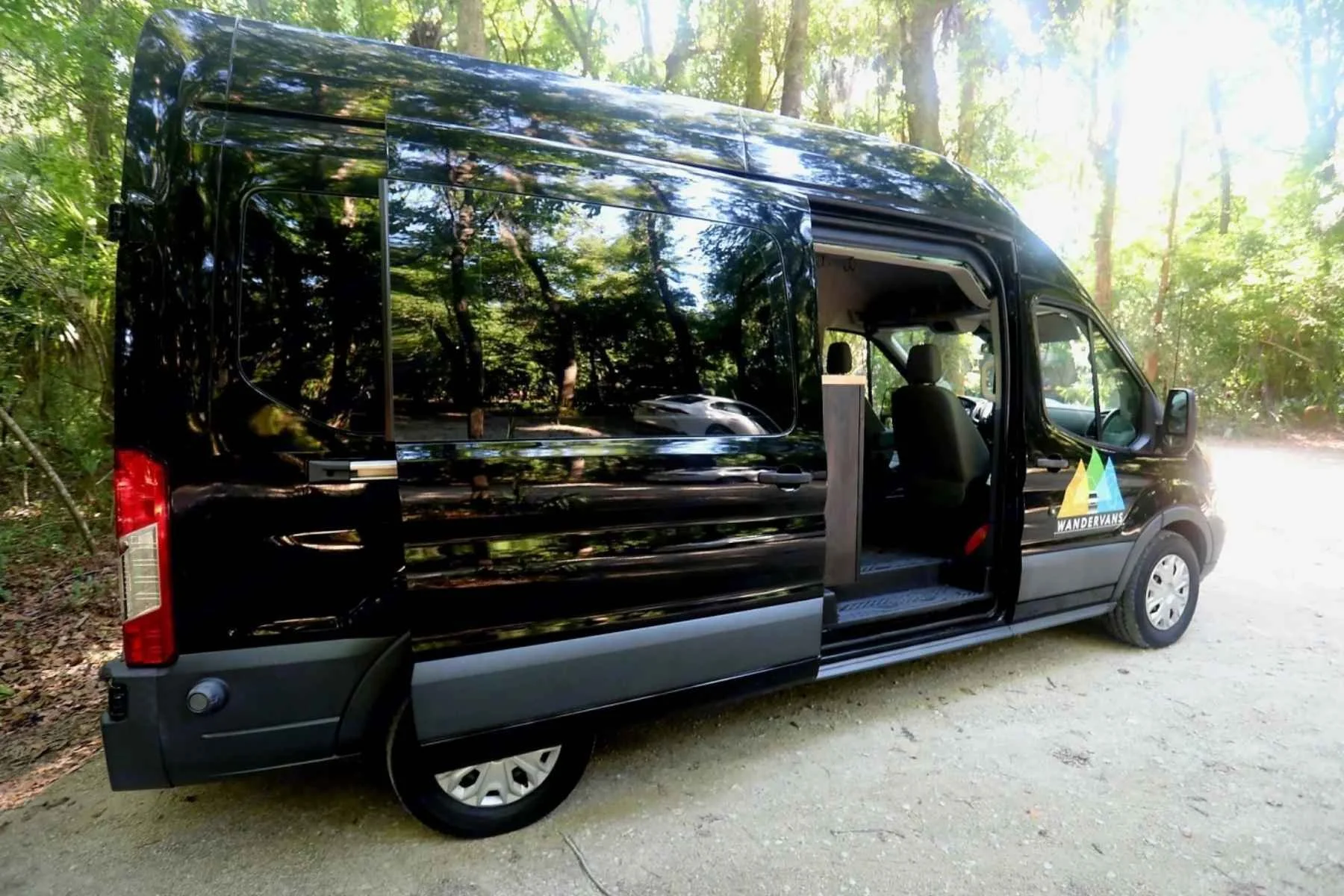 Best budget camper van in South Carolina parked in a shaded forest campsite, featuring a sleek black high-roof conversion van with the sliding door open and a simple, practical interior..