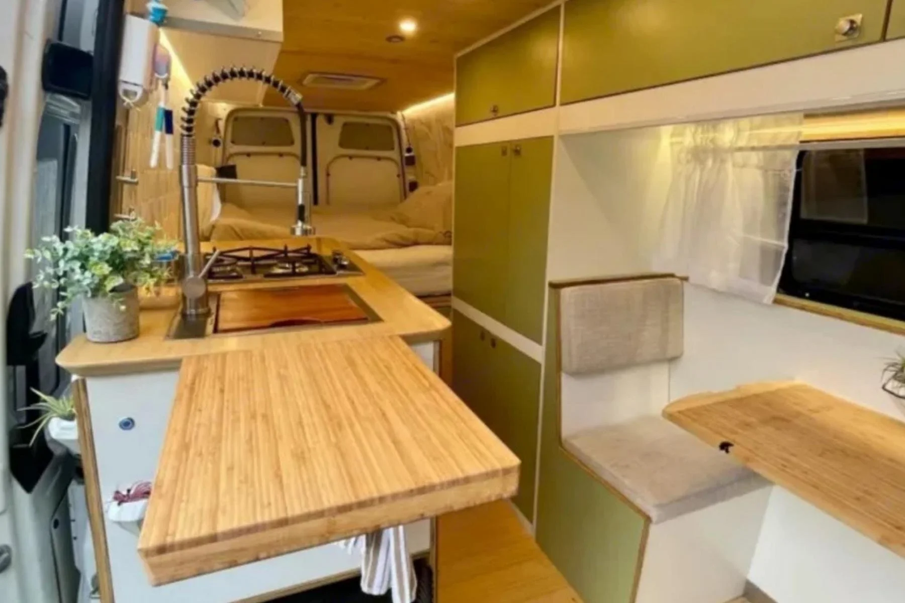 Interior of 'Sage the Mercedes' camper van rental in Las Vegas, featuring a sage green kitchen, wooden countertops, a cozy queen bed, and a built-in dining nook for couples.