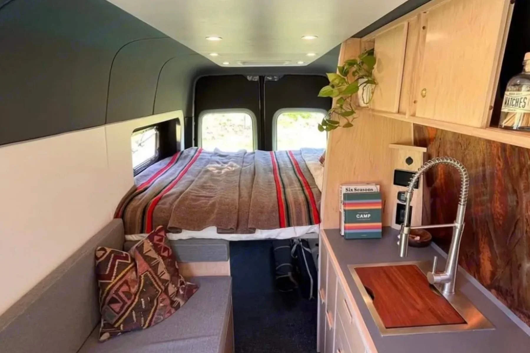 Luxury Sprinter conversion van interior with solid wood cabinetry, premium bedding, and modern kitchenette.