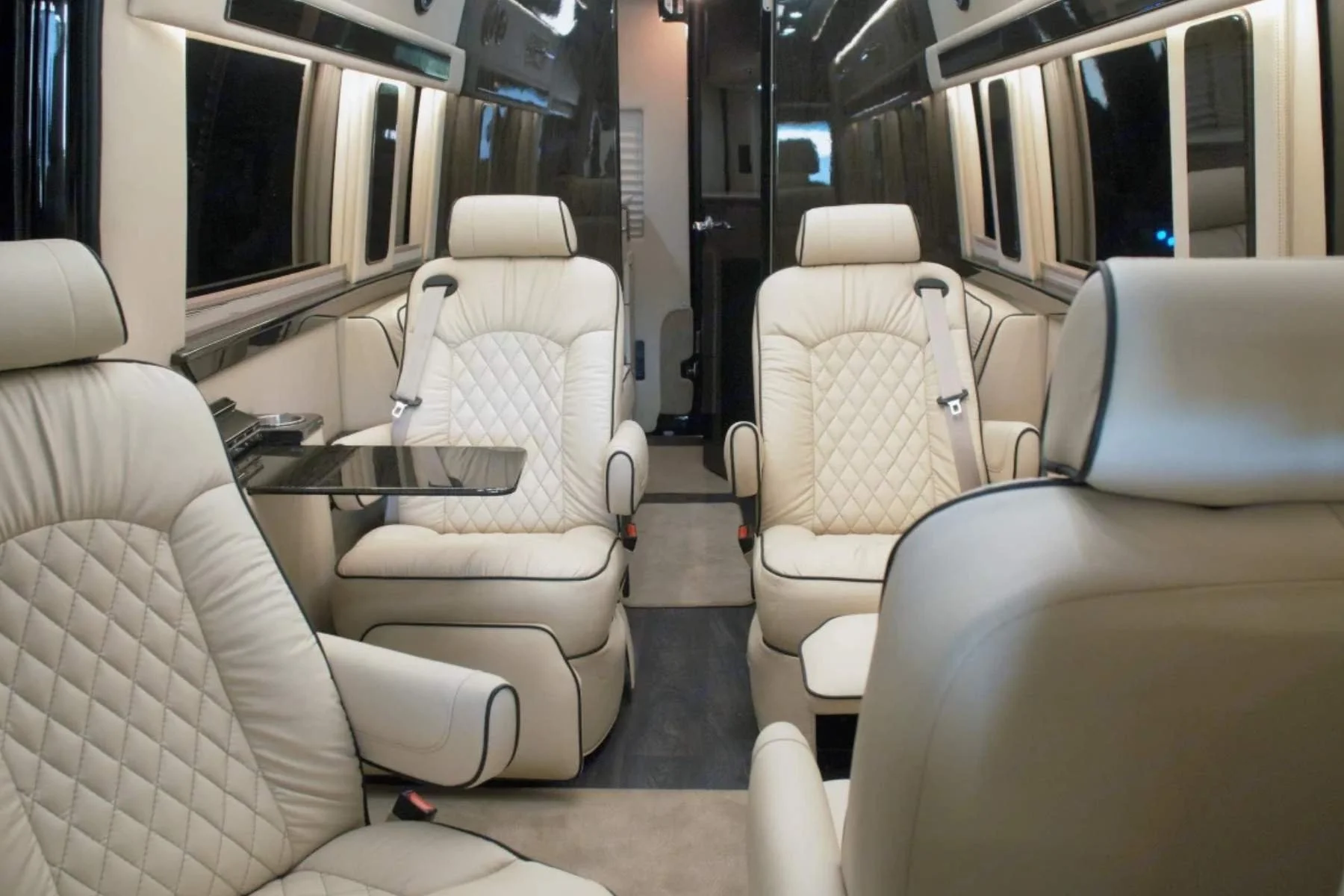 Cream diamond-stitched captain's chairs facing a fold-down table inside a Midwest Automotive Designs rental