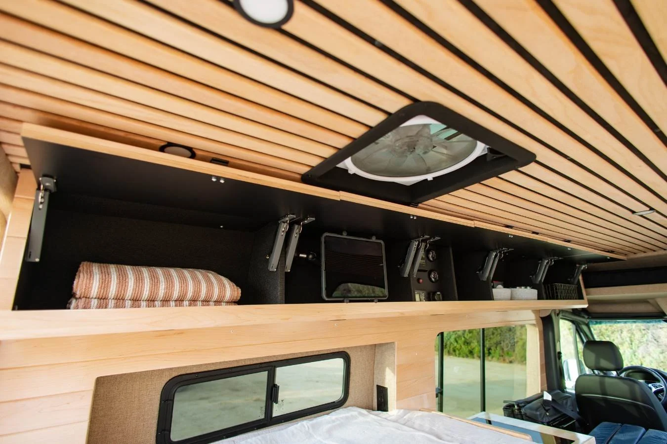 Upper storage shelf above bed in modern luxury camper van interior.