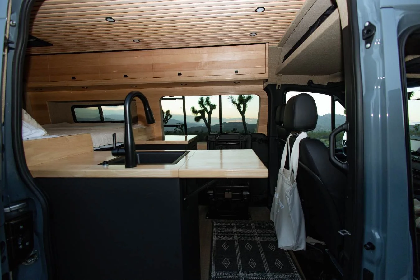 Modern kitchenette inside luxury camper van with sink, cabinets, and scenic window views.