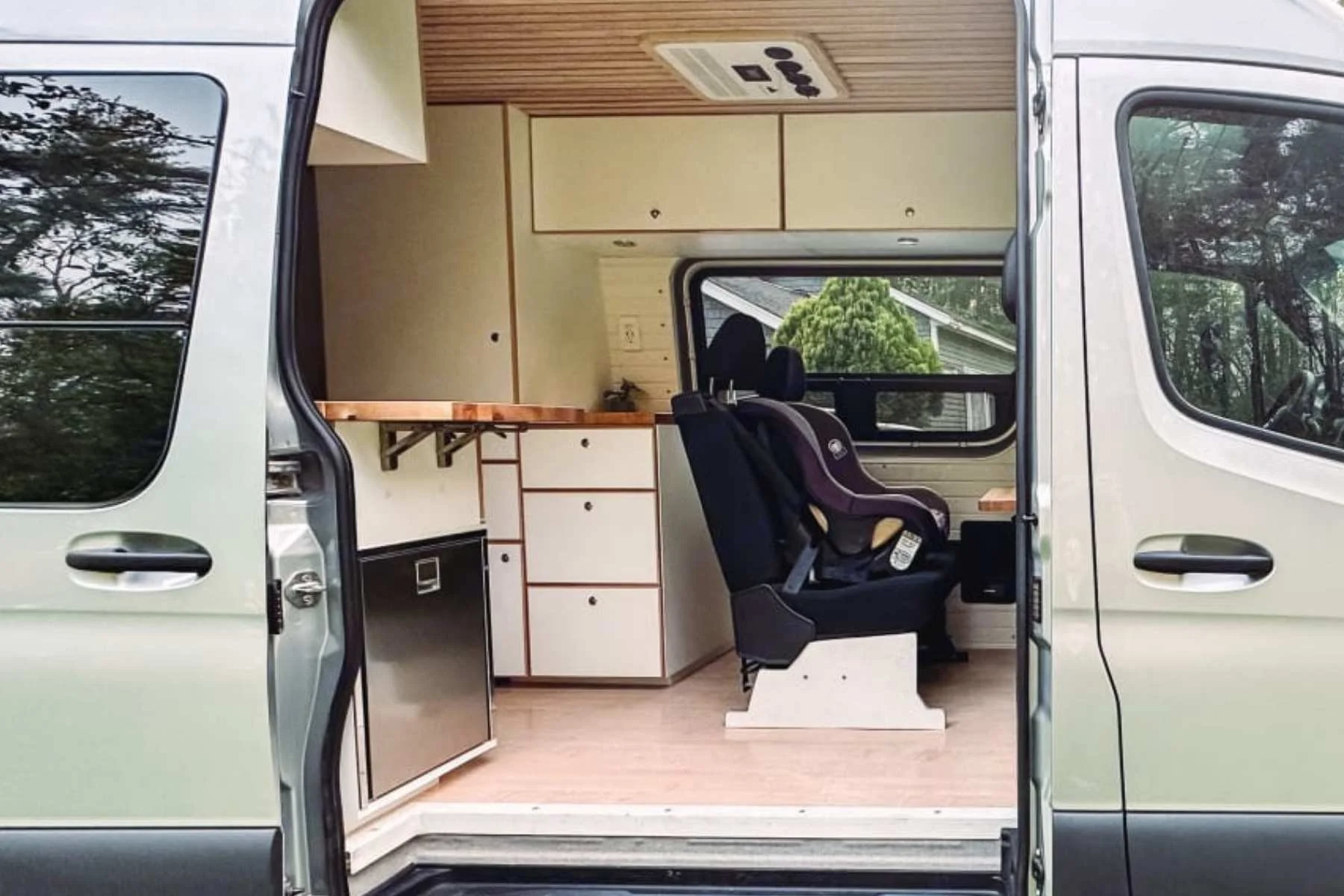 Pet-friendly Sprinter van interior with open sliding door, kitchenette, and rear seating for travel with dogs.