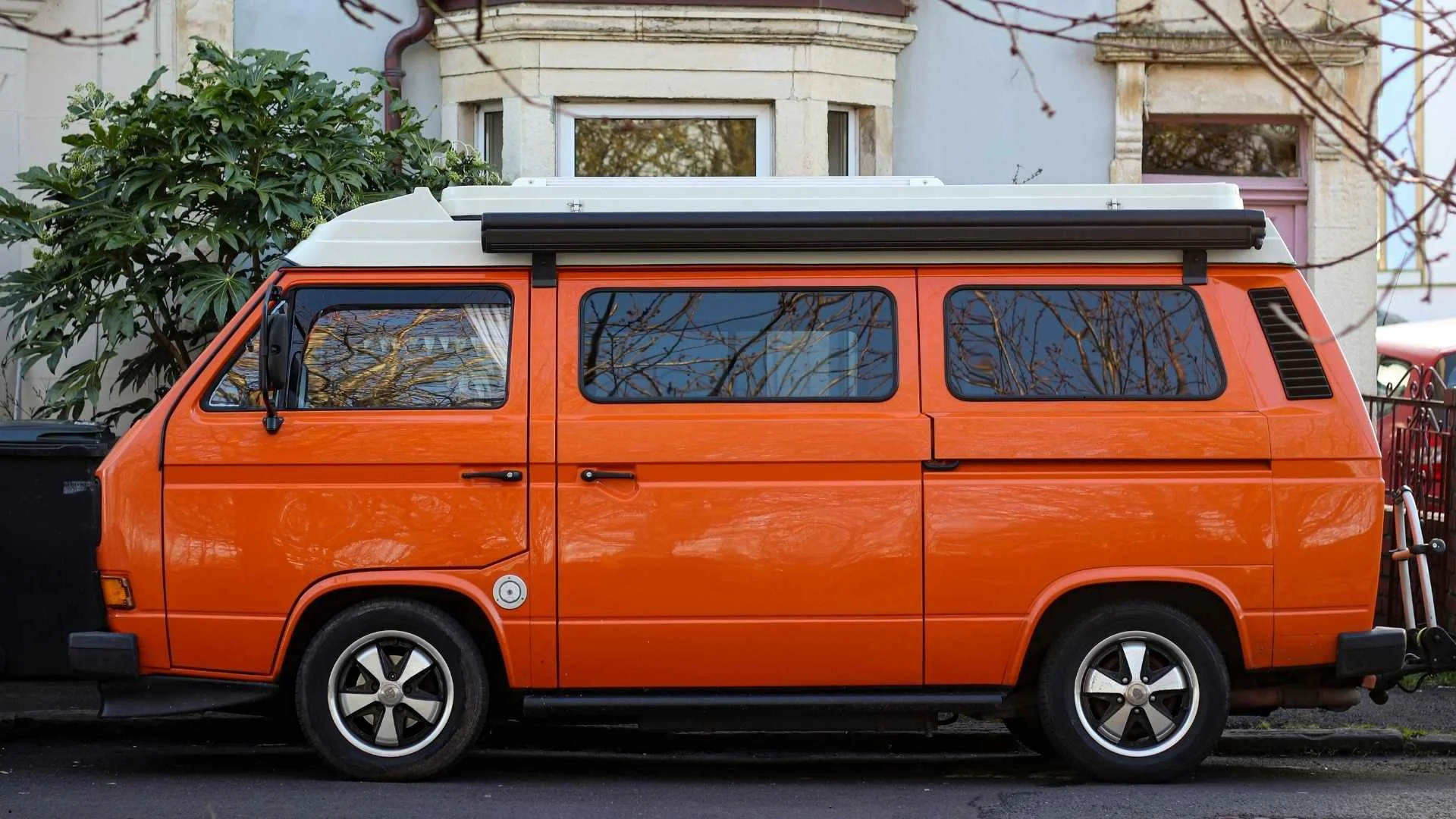 Orange Volkswagen Vanagon with a pop-top roof parked on a residential street — available through vanagon rentals on altCamp.com