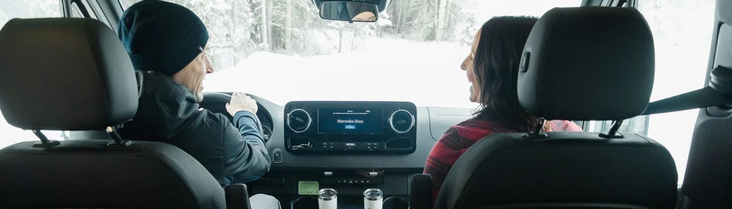Couple in the front seats of a Mercedes-Benz Sprinter on a snowy road