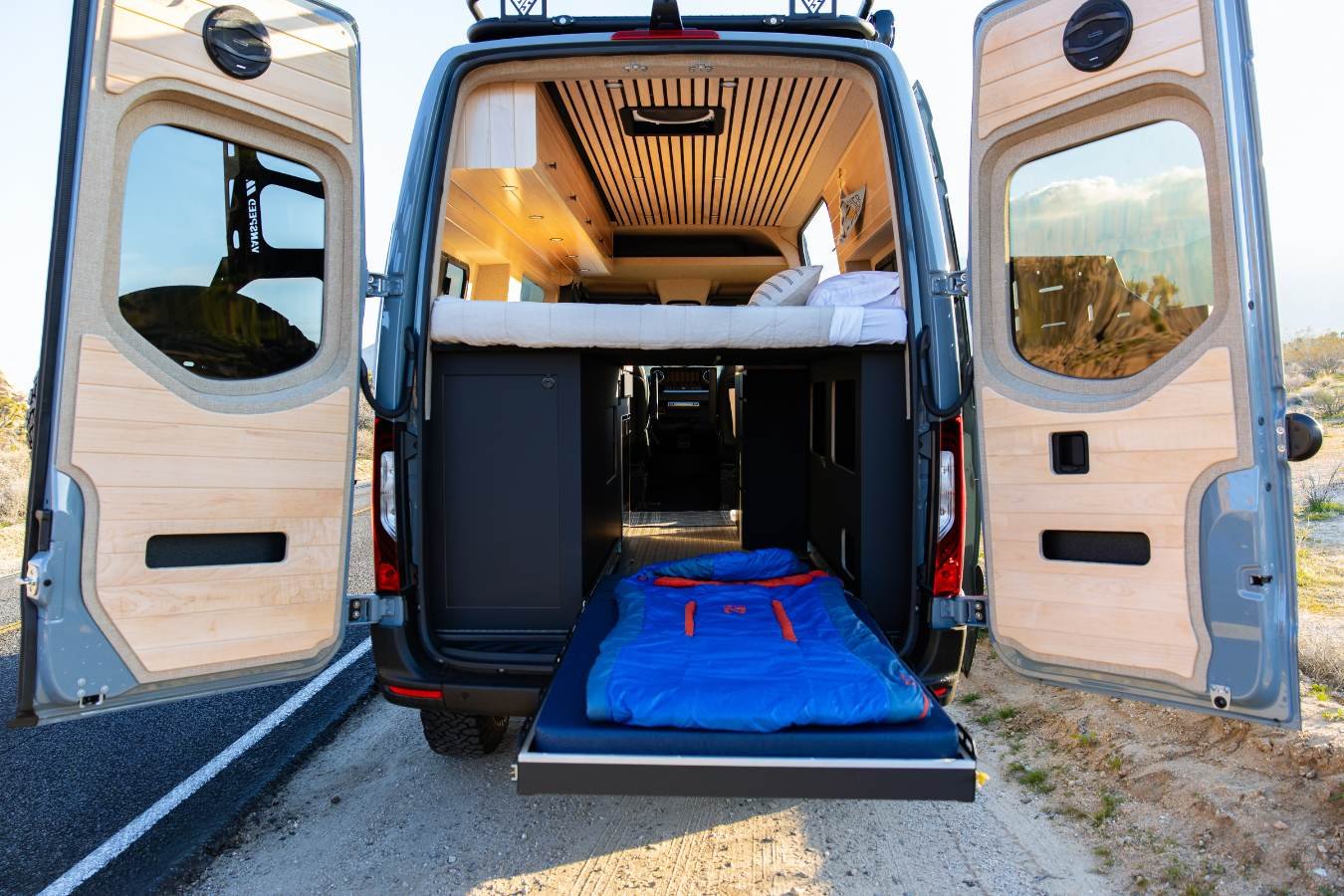 Open rear cargo area with gear storage and sleeping setup in luxury camper van rental