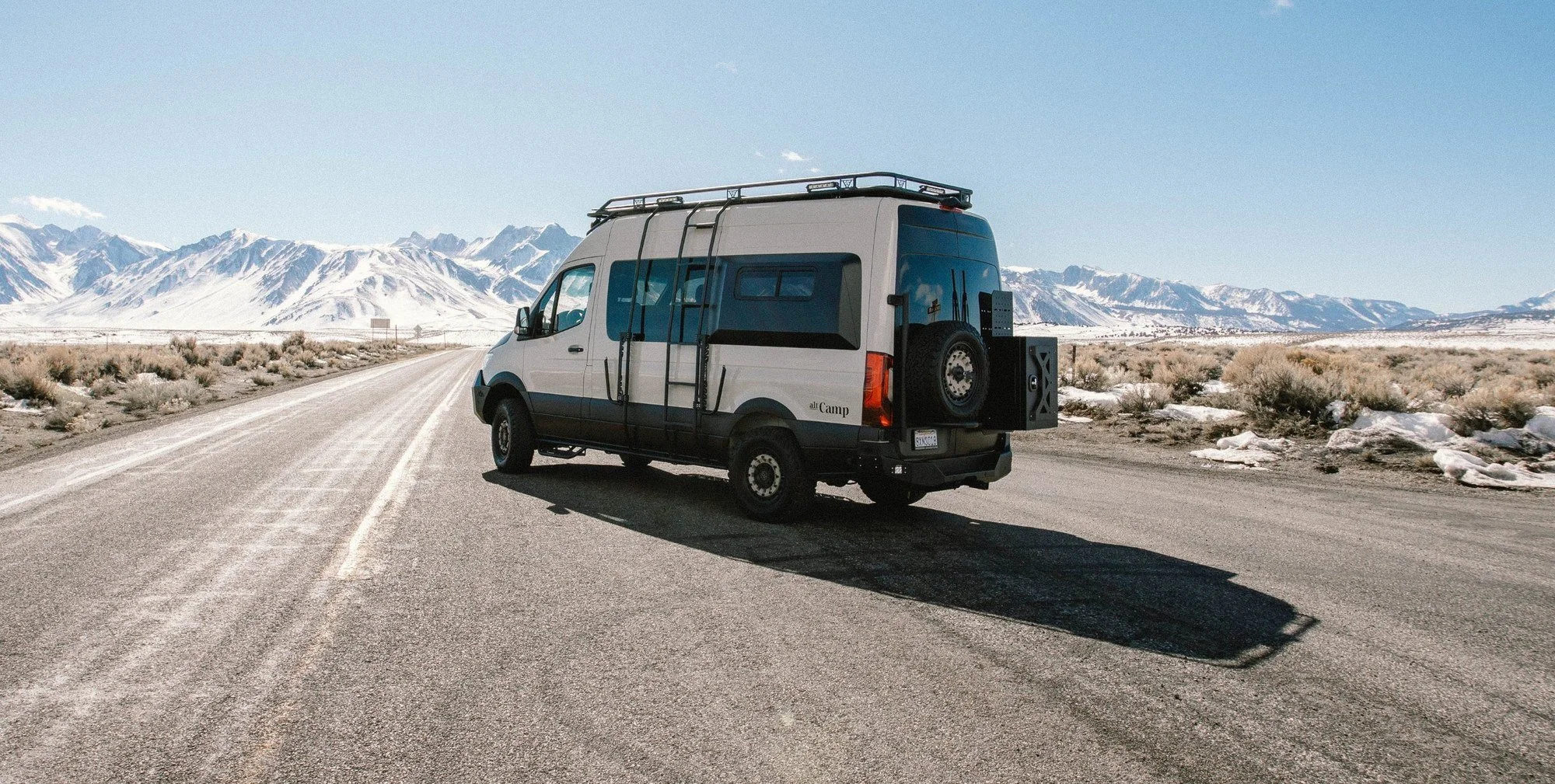 Camper van on a high desert road with snow-capped Sierra mountains