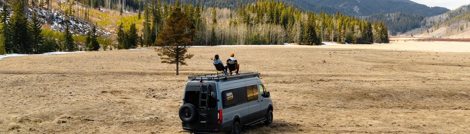 Couple sitting on the roof of a camper van in a Colorado meadow with mountains