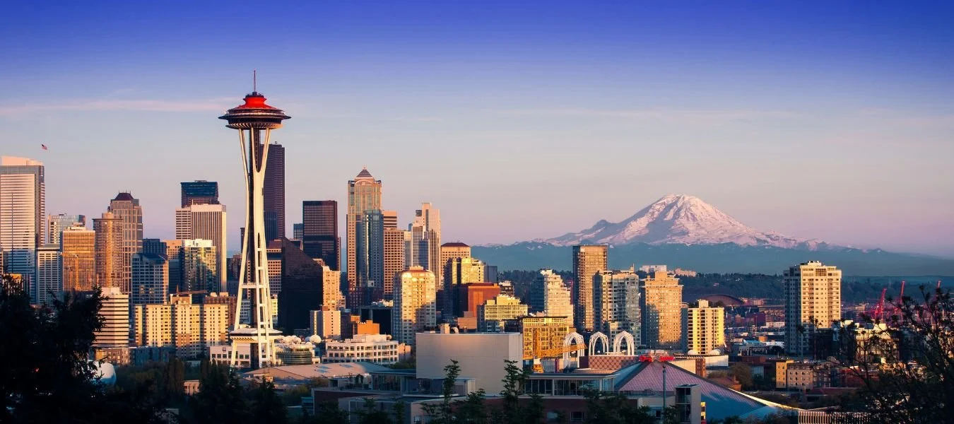 Downtown Seattle skyline at sunset with the Space Needle and Mount Rainier behind it, the starting point for van rental trips into the Cascades and Olympic Peninsula.