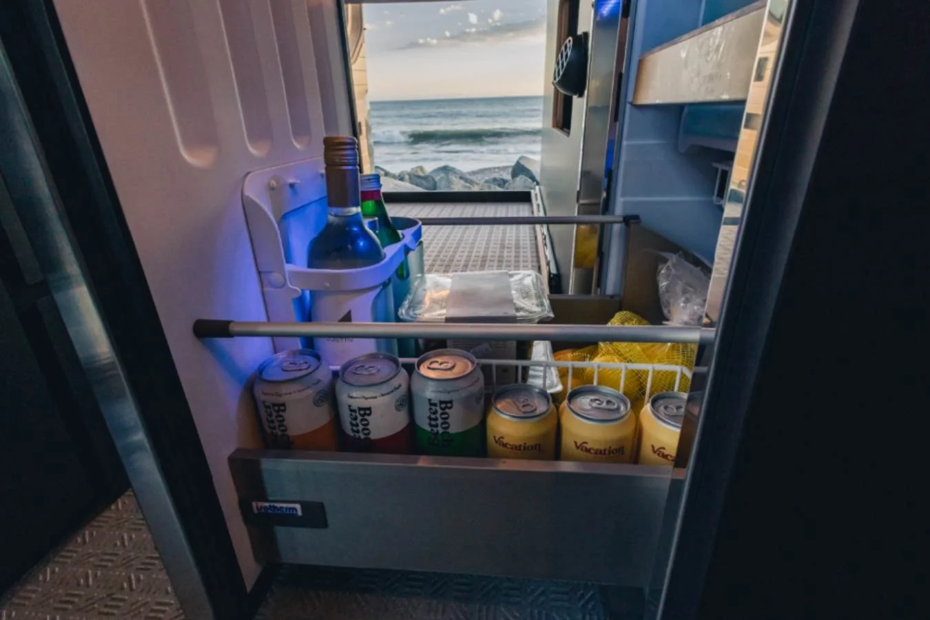 Built-in refrigerator stocked with drinks inside premium Sprinter camper van.