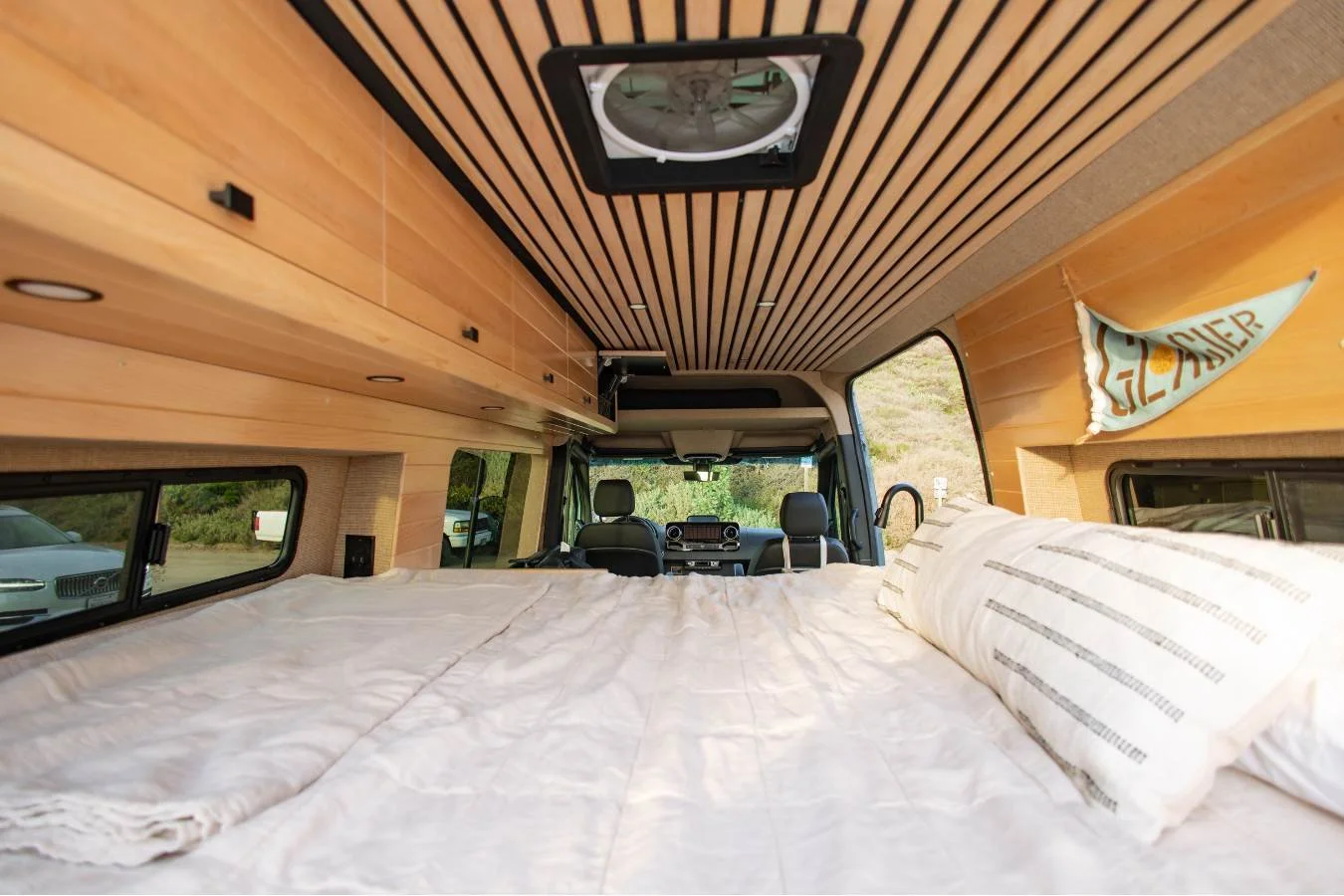 Wide rear bed with wood slat ceiling inside luxury Mercedes Sprinter camper van.