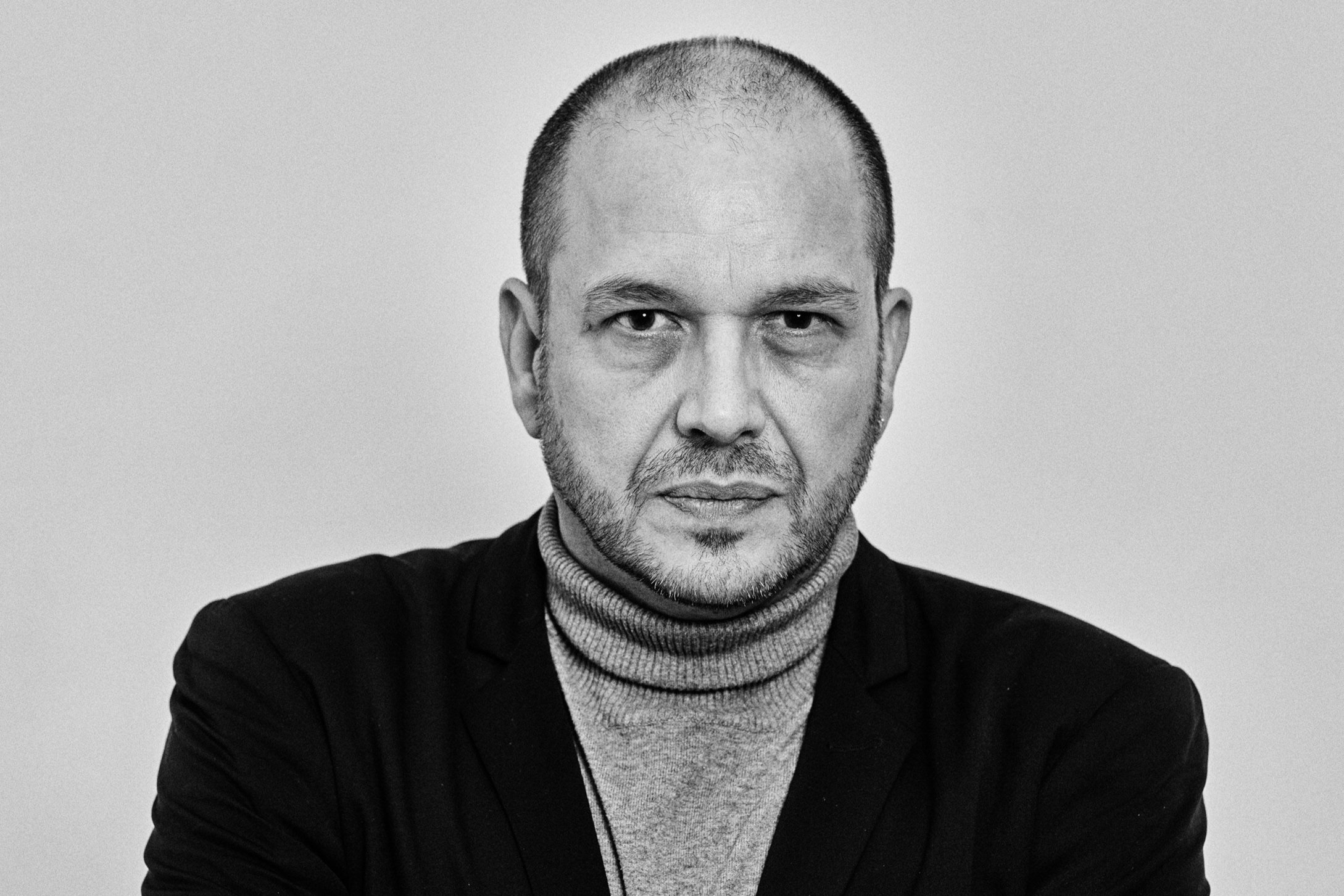 Black and white portrait of a man in a turtleneck and blazer.