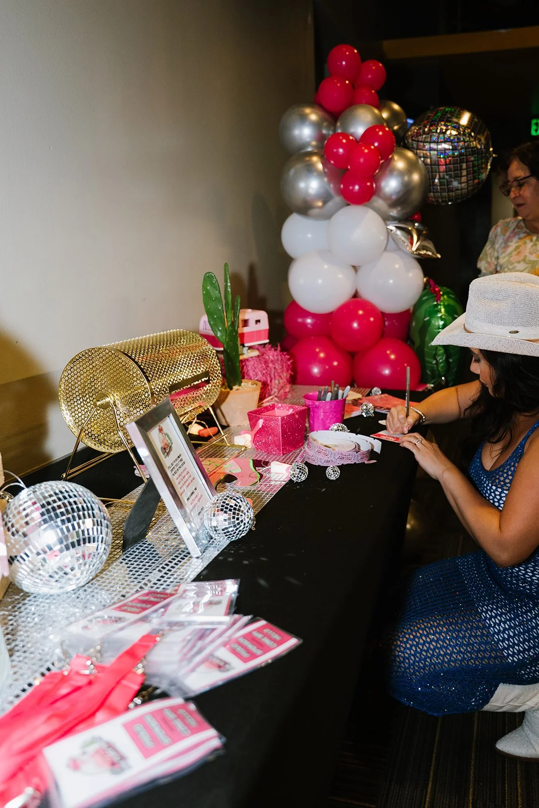 A decorated table with pink, white, silver, and gold balloons, disco balls, and party supplies at a celebration or party.