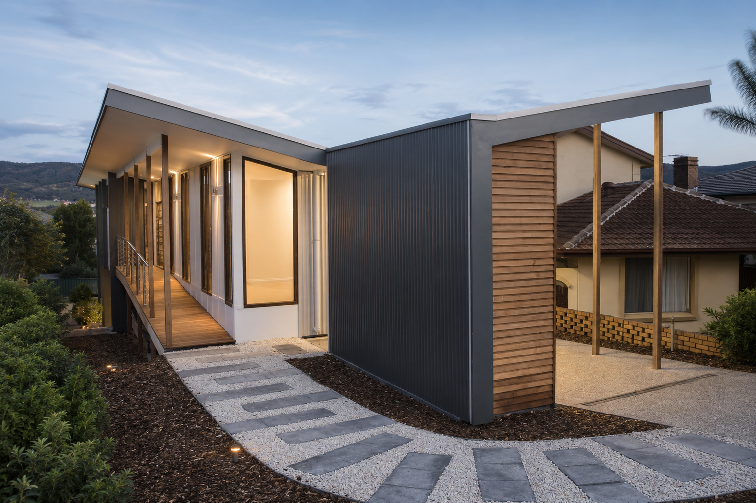 Modern house with a curved pathway leading to the entrance, featuring a mix of wood and metal siding, large glass windows, landscaped garden, and a sky with scattered clouds at dusk.