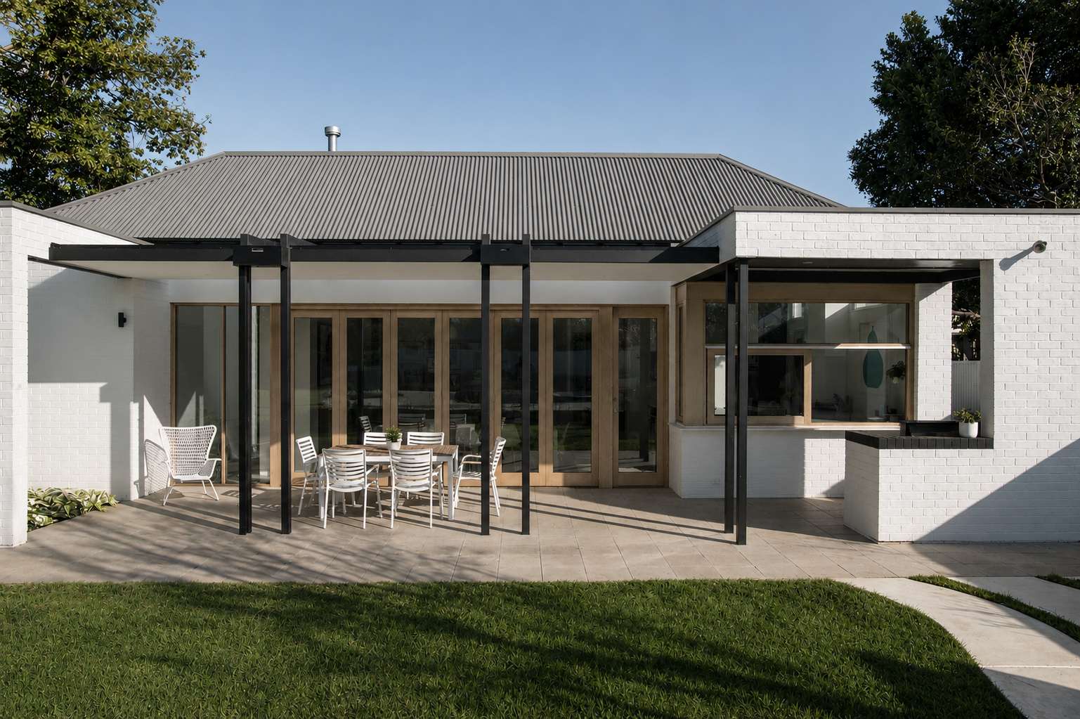 Modern house with outdoor patio, white brick walls, glass doors, wooden trim, black steel support beams, patio furniture, and a small grassy yard.