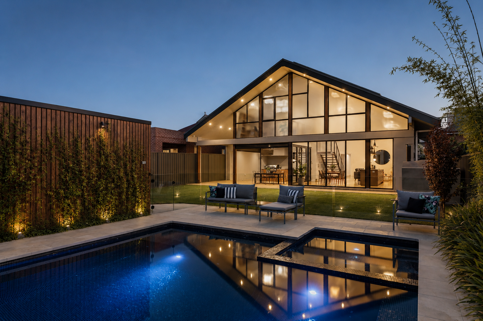 Modern house with large glass windows, outdoor seating area, and swimming pool at dusk