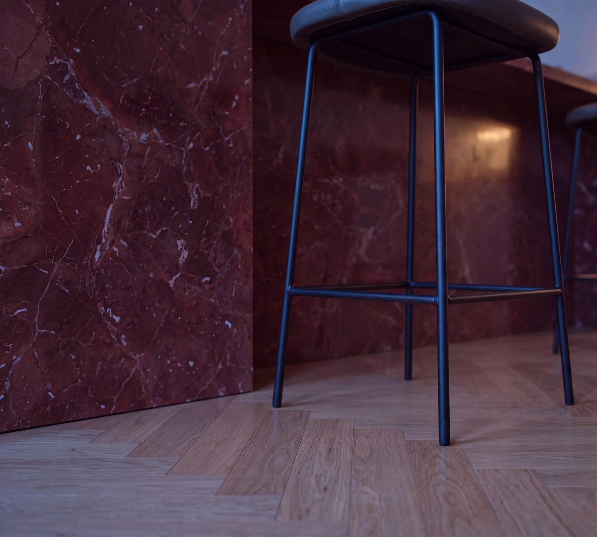 Dettaglio di un rendering 3D fotorealistico di una cucina parigina, con isola rivestita in marmo rosso, sgabello nero e pavimento in parquet.