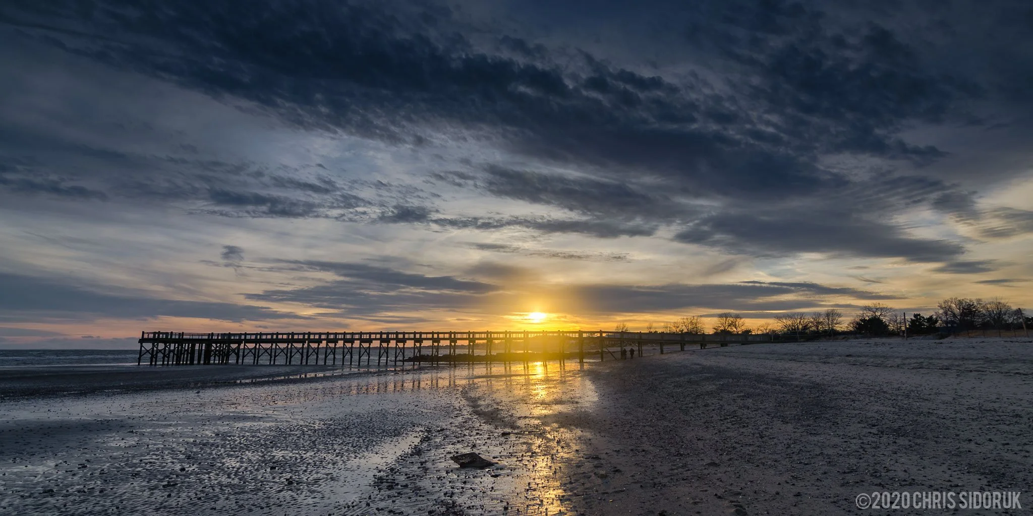 Sunset over the Walnut Beach pier in Milford, Connecticut, with warm light reflecting on the water.