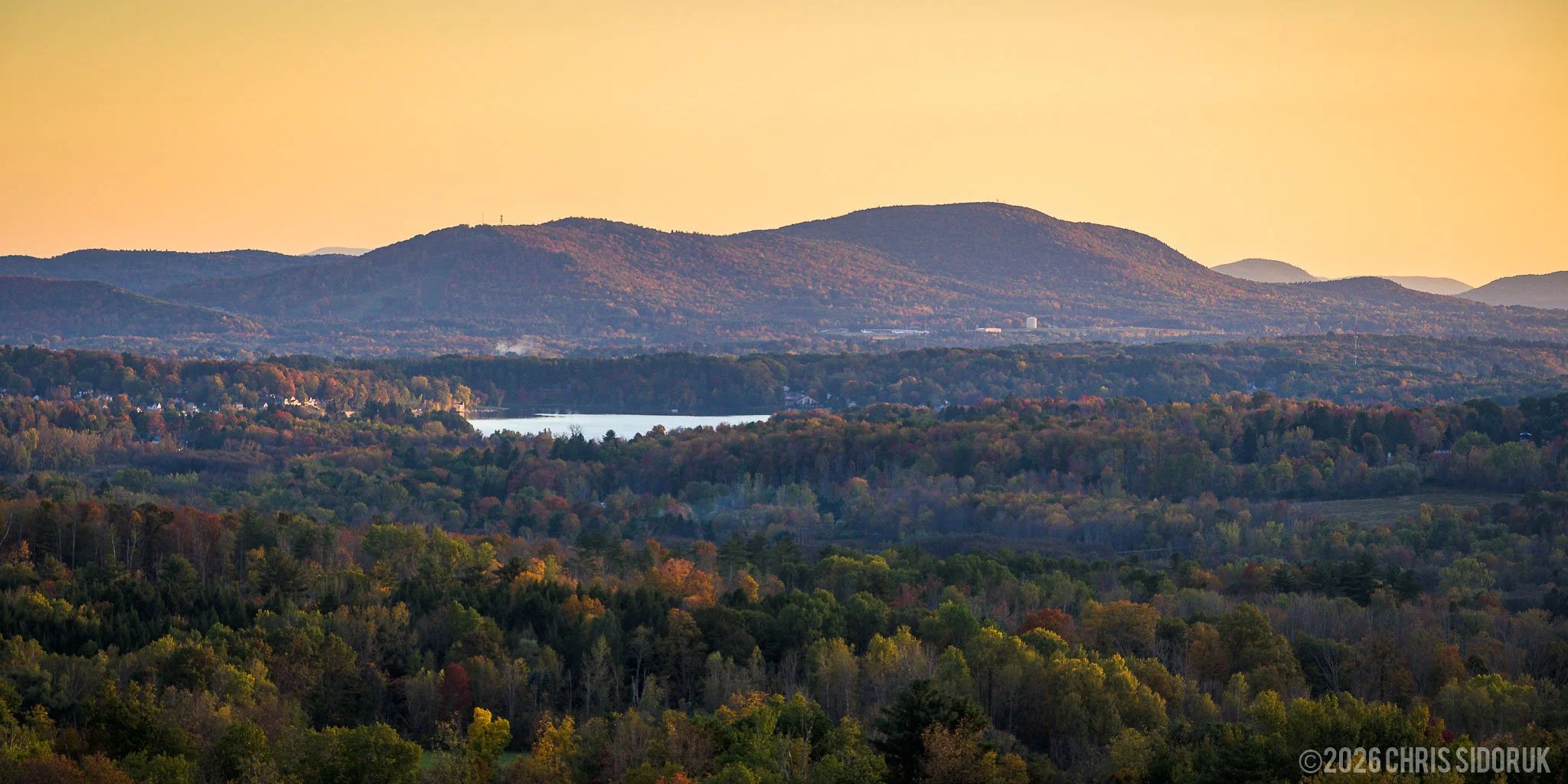 View from Mount Greylock over the Berkshires at sunset with layered hills, fall foliage, and a distant lake in Massachusetts.
