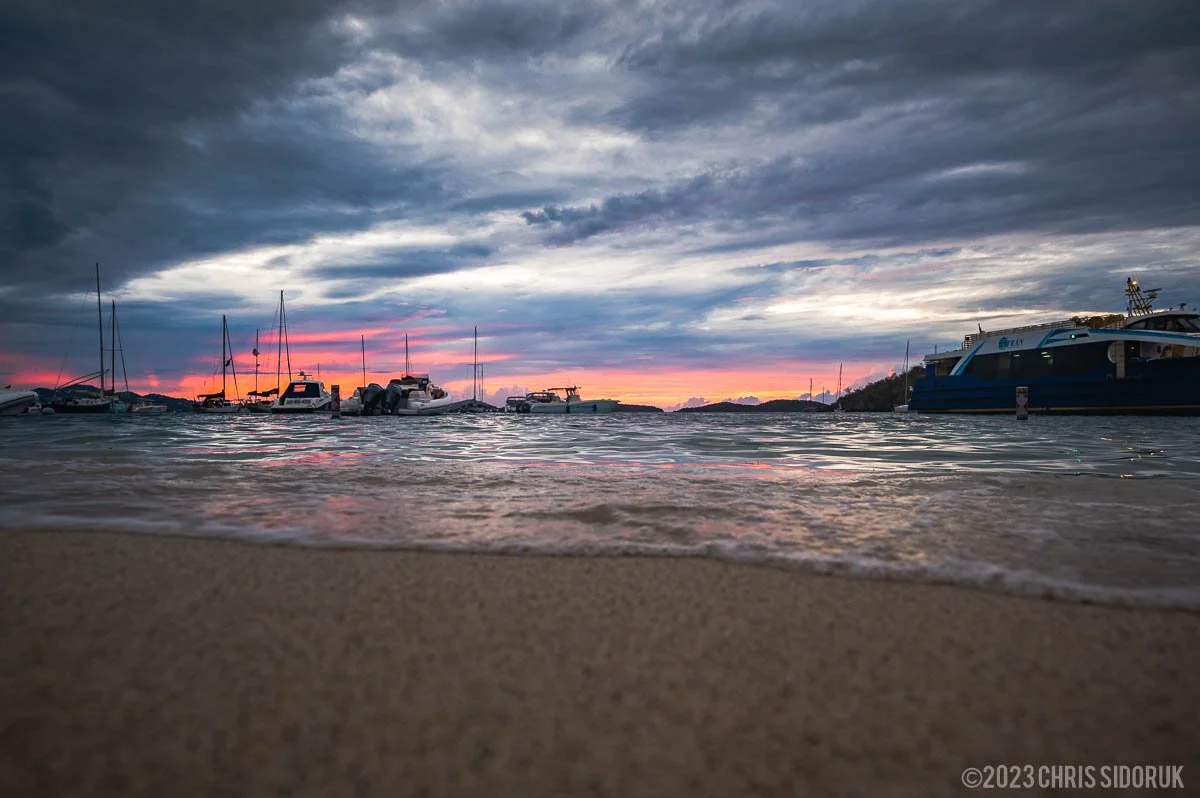 Sunset shoreline in St John USVI with boats anchored in calm water and dramatic evening sky