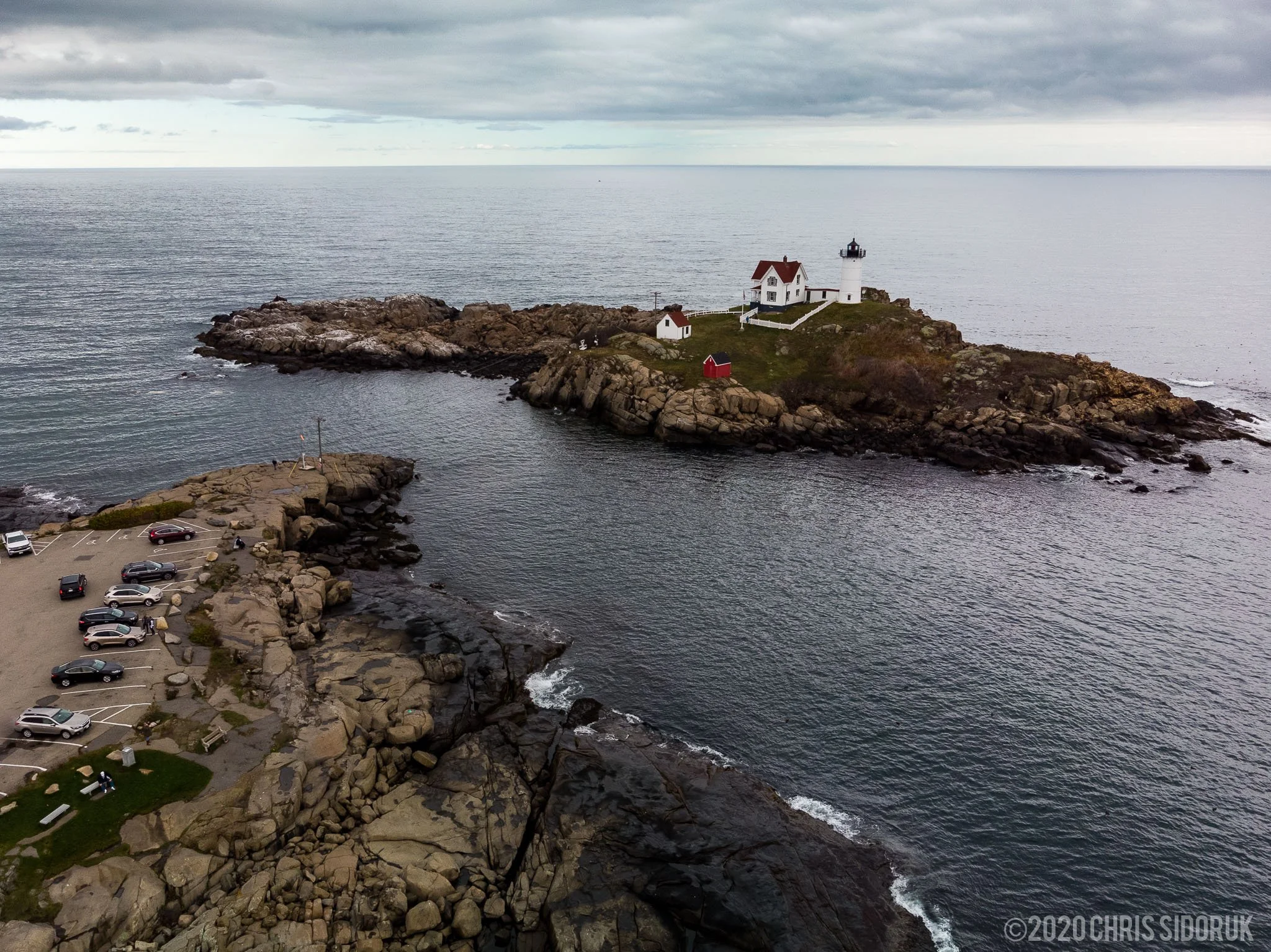 Aerial view of Nubble Lighthouse in York, Maine showing the rocky coastline, parking area, and surrounding Atlantic Ocean.