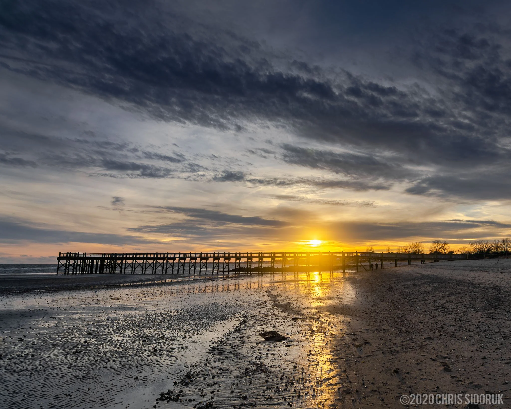 Sunset behind wooden pier at Walnut Beach in Milford, Connecticut with reflections across wet sand at low tide