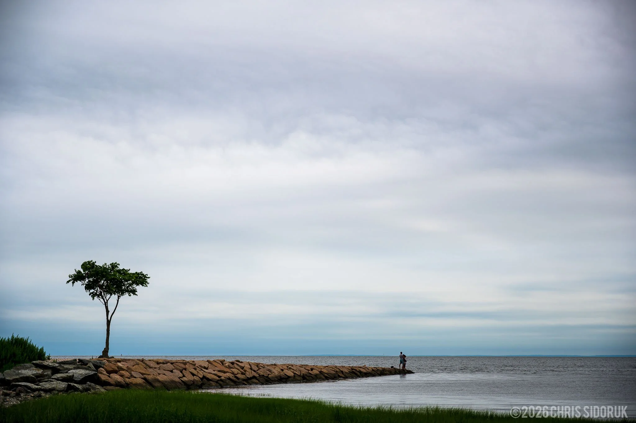 Rock jetty extending into Long Island Sound at Walnut Beach in Milford, Connecticut with calm coastal water and overcast sky