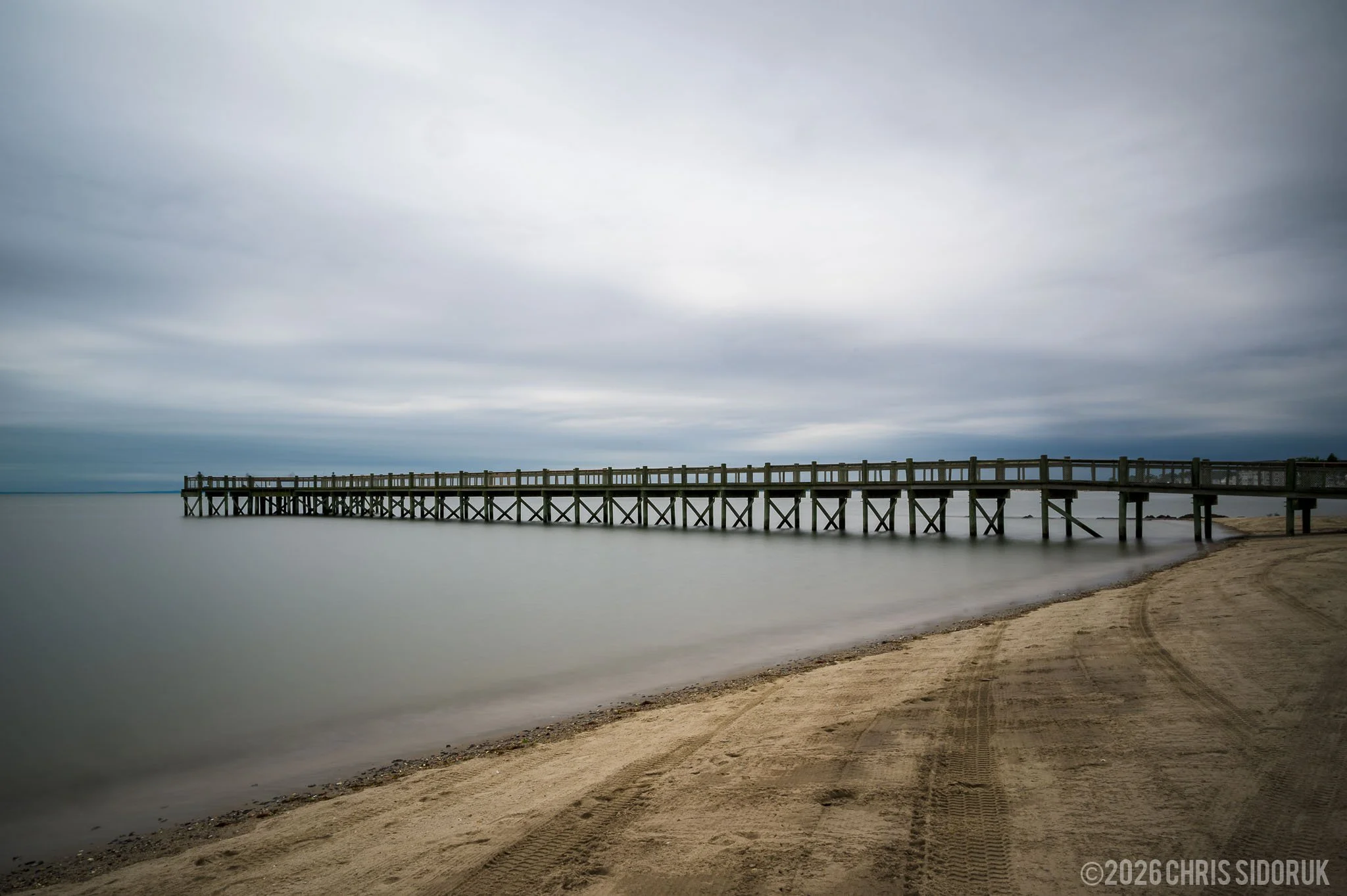Long exposure of the Walnut Beach pier extending into calm water in Milford, Connecticut under a soft overcast sky