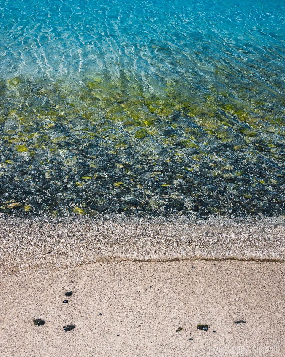 Clear Caribbean water meeting sandy shoreline in St John USVI with visible rocks beneath the surface