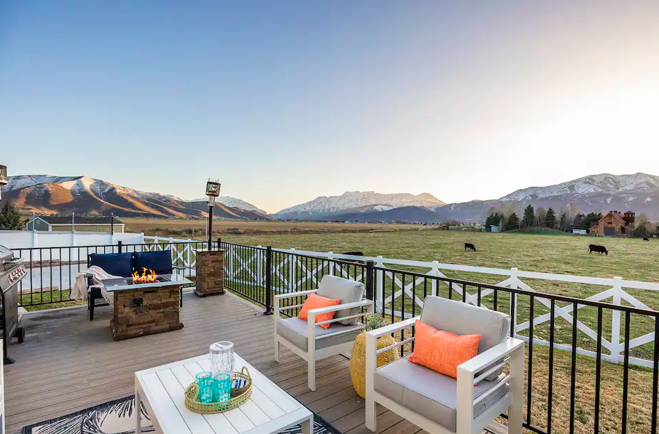 Patio with outdoor furniture, fire pit, and mountain view with snow-capped peaks and grazing horses.