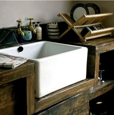 Rustic kitchen with a white farmhouse sink, wooden countertops, dish rack, and various kitchen items.