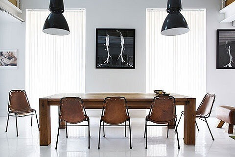 Modern dining room with a wooden table, six leather chairs, black pendant lights, and framed artwork on the walls.