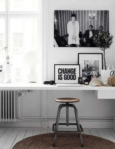 Minimalist white workspace with a stool, framed art, and plants