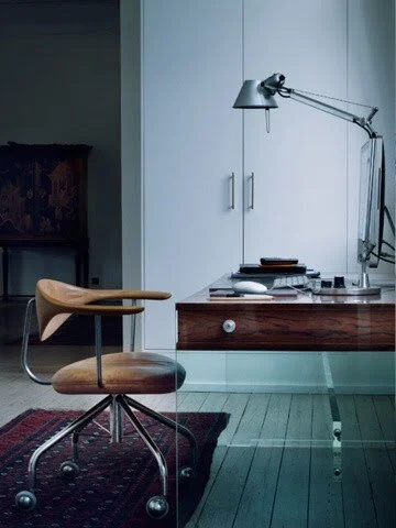 Modern home office with a wooden chair, glass desk, anglepoise lamp, and sleek computer setup.