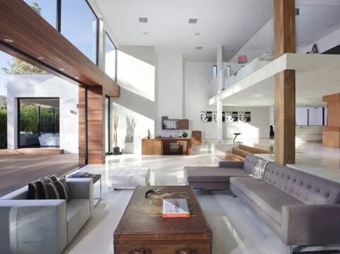 Modern open-concept living room with large windows, gray sofas, wooden coffee table, and balcony.