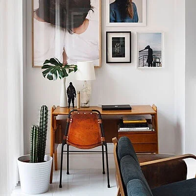 Modern home office setup with wooden desk, leather chair, potted cactus, and framed artwork on the wall.