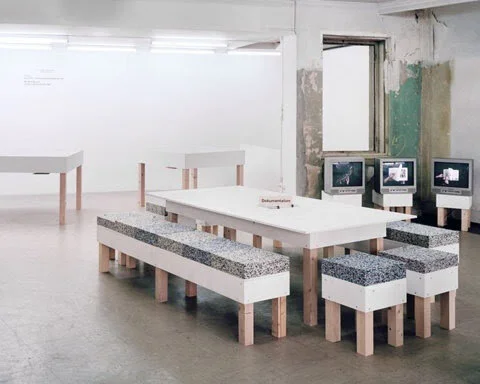Interior with modern table and benches, multiple monitors displayed; minimalistic design, gray and white color scheme.