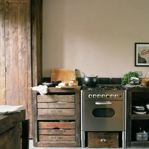 Rustic kitchen interior with wooden crates, a modern stainless steel stove, cooking ingredients, and a small framed picture on the wall.