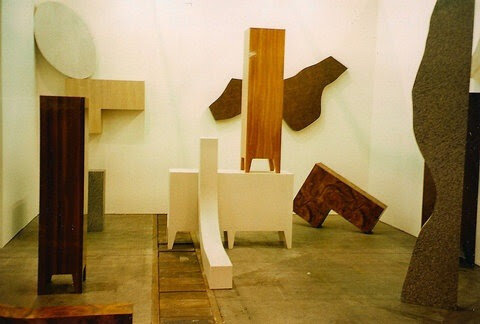 Abstract art installation featuring various geometric wooden sculptures in a gallery space, with a variety of shapes and textures.
