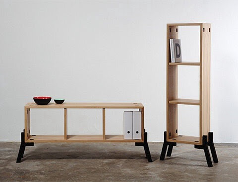 Minimalist wooden shelf set with black legs, featuring open compartments. One piece is a low bench serving as storage, holding bowls and books. The other is a tall, narrow shelving unit with books and decorative items.