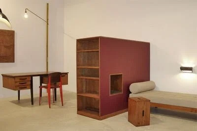 Mid-century modern office with wooden desk, red chair, bookshelf, and bench. Minimalist design.