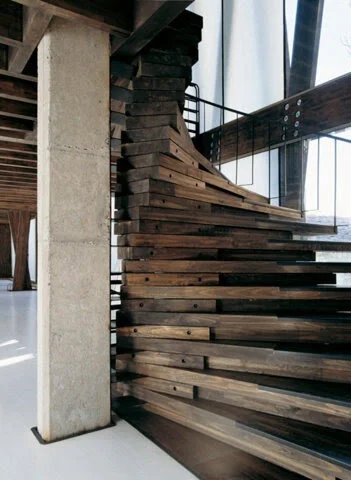 Modern wooden staircase with a unique curved design structure adjacent to a concrete wall in an industrial-style interior.