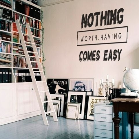 A room with a tall bookshelf, a ladder, and various framed art. The wall has a quote that says "Nothing worth having comes easy." There's a desk with items including a globe and a candlestick.