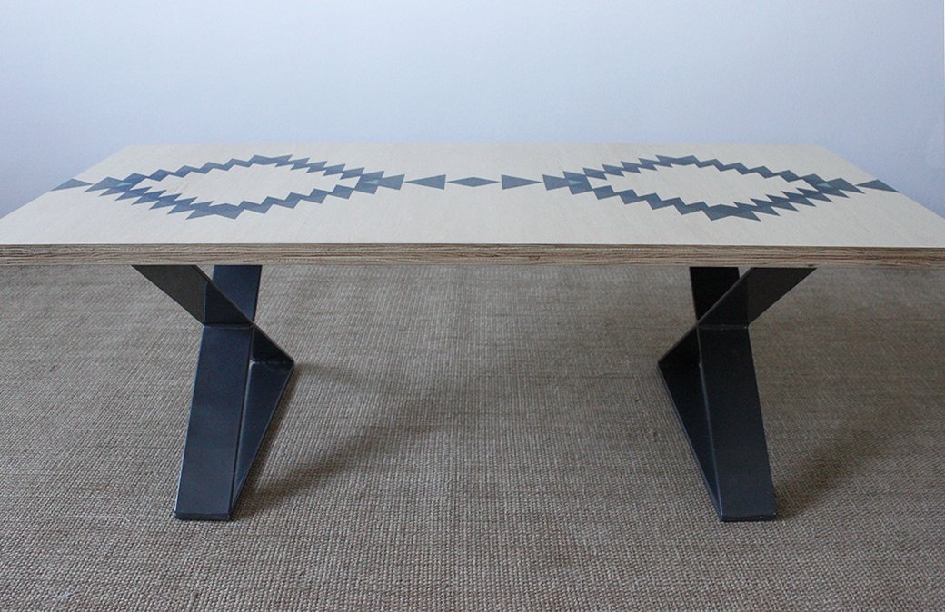 Modern wooden coffee table with geometric pattern on top and metal legs, placed on a carpet.