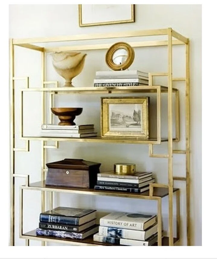 Gold-colored shelving unit with decorative items, including framed art, books, vases, and a small wooden box.
