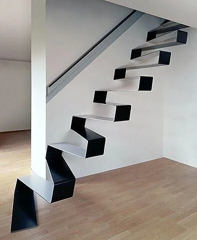 Modern minimalist staircase with black and white zigzag design in a room with light wooden flooring.
