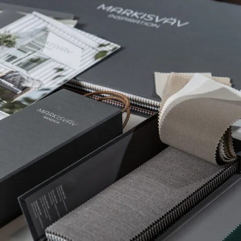 Prover på olika markisvävar och tyger på ett bord, med broschyrer och materialprover i bakgrunden.