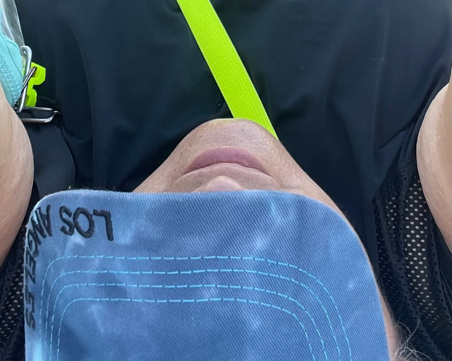 Pov of laying down selfie with light blue Los Angeles cap neon yellow strap across chest