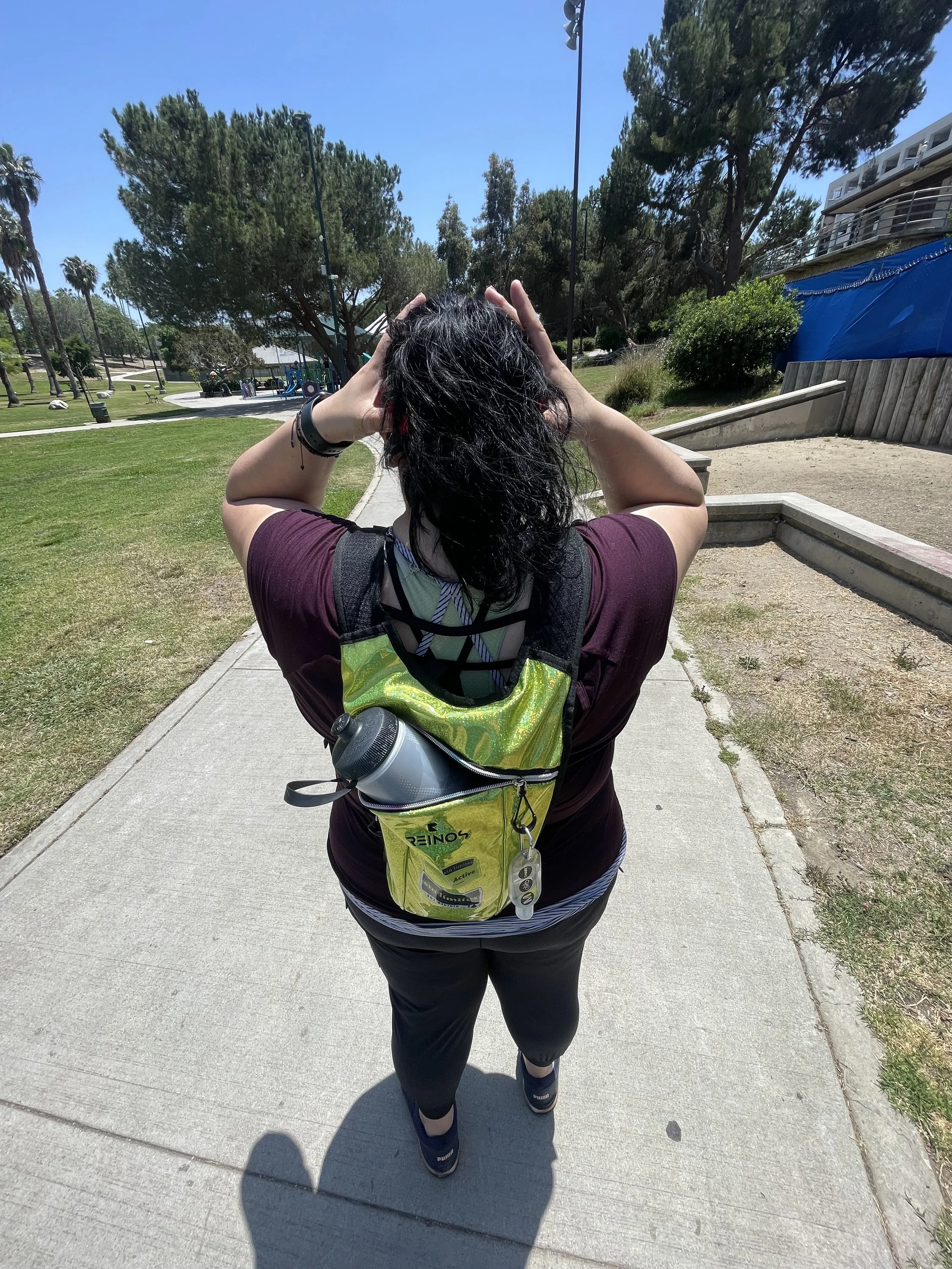 Coach Vida pony tail burgundy active shirt with a neon yello backpack standing looking forward