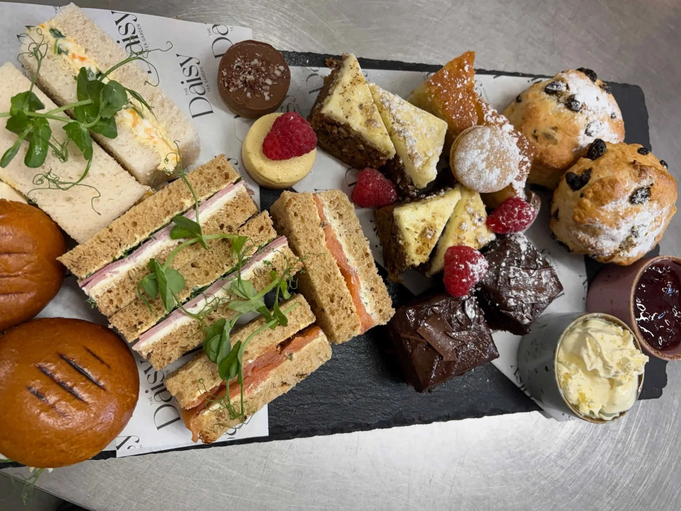 Assorted finger sandwiches, mini cakes, muffins, and chocolates on a platter at a tea party.